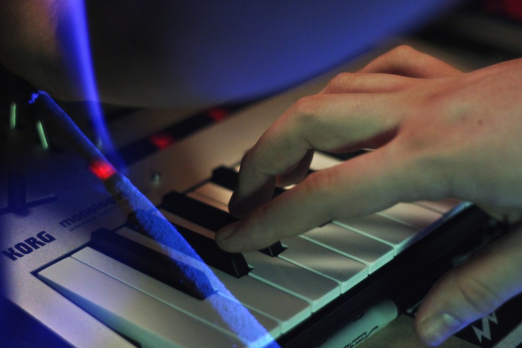 Korg Monologue synthesizer being played, overlaid with image of incense.