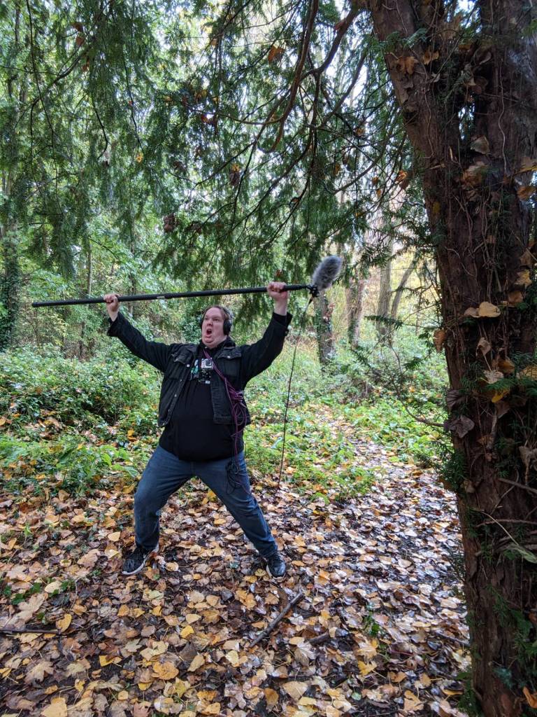 Sound recordist cheering heroically in a forest, holding a boom pole above his head