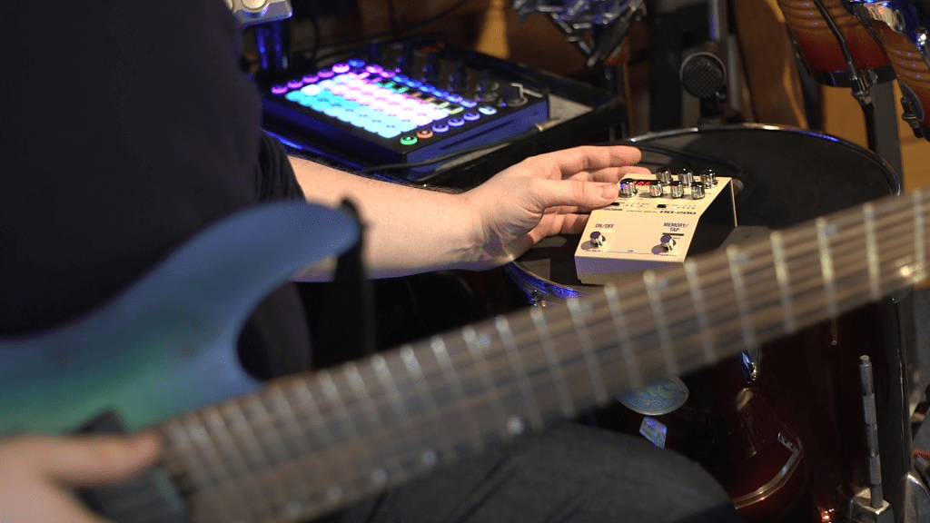 Man holding an 8-string guitar adjusts the settings on a Boss DD-200 delay pedal.